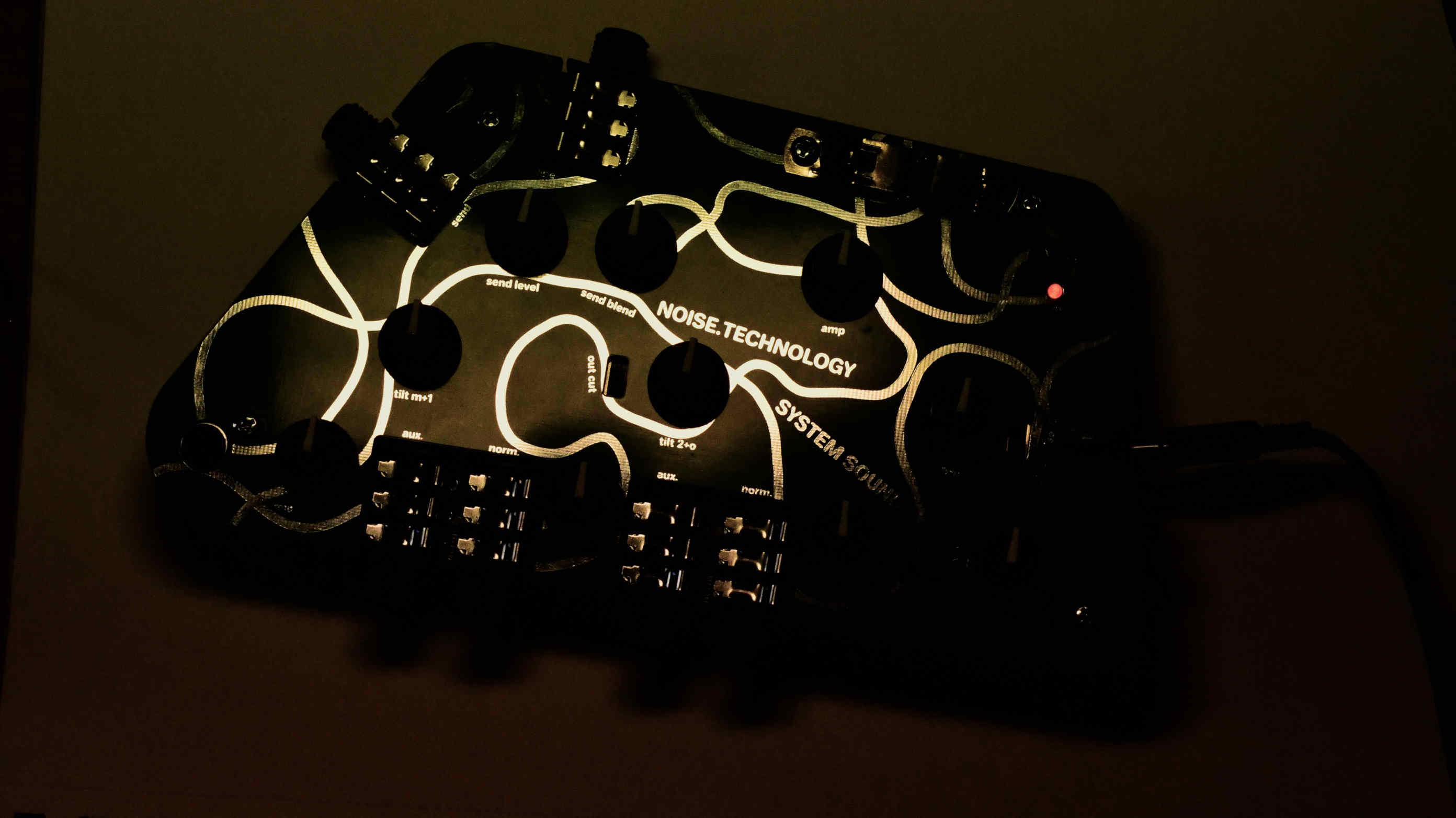 System Sound System Sound. A pcb device in the dark, with golden light making curvy lines and various labels and System Sound shine.